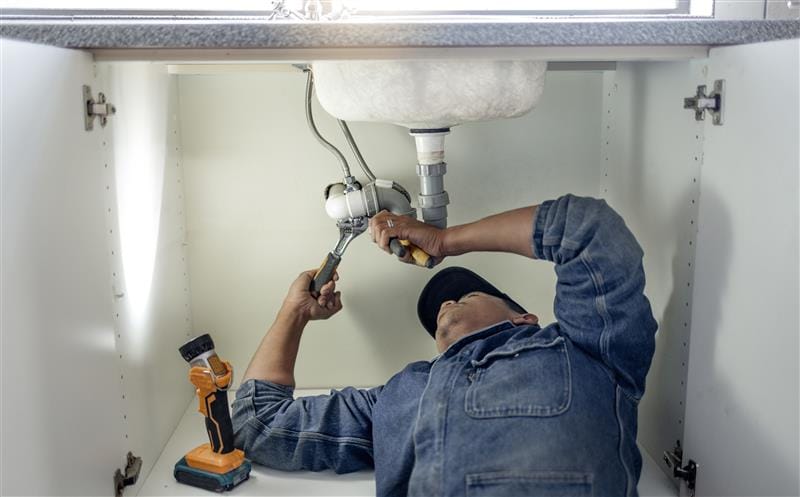 Plumber repairing pipes beneath a bathroom sink in Naples