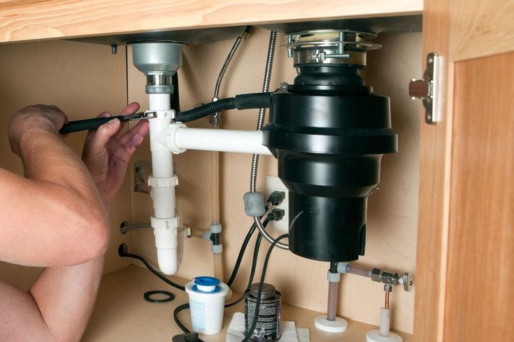 Plumber installing a garbage disposal beneath a kitchen sink in Naples