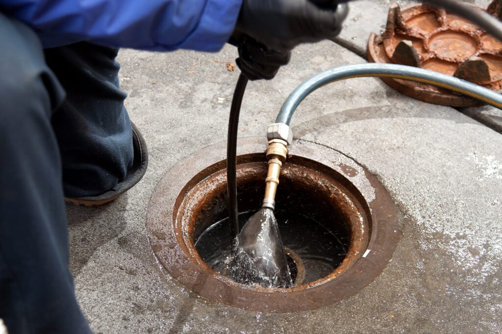 Plumber hydro jetting a sewer line through a manhole in Naples