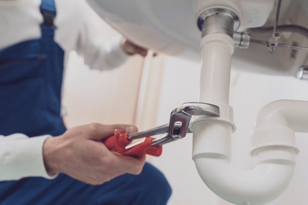 Plumber repairing a white drain pipe beneath a sink in Naples