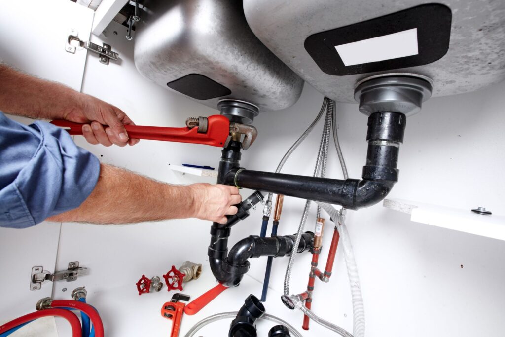 Plumber repairing drain pipes beneath a kitchen sink in Naples